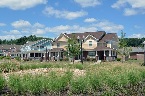 Row of modern townhouses with brick columns and landscaped front yards along a quiet residential street under a clear blue sky.
