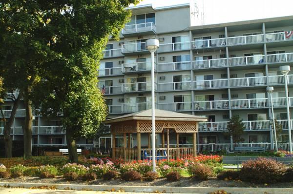 A multi-story apartment building with balconies is behind a wooden gazebo surrounded by trees, bushes, and flowers.