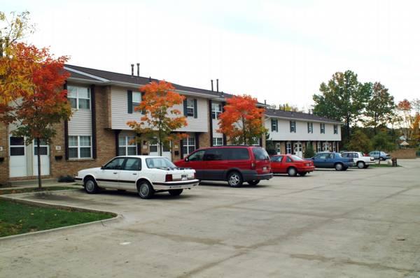 A row of two-story townhouses with cars parked in front. Trees with autumn foliage line the sidewalk.