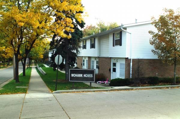 Two-story apartment buildings with a sign reading "Mohawk Homes," autumn trees, a sidewalk, and a pink bicycle near the entrance.