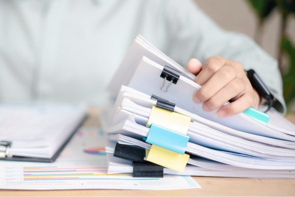 A person organizes stacks of paper documents bound with binder clips on a desk.