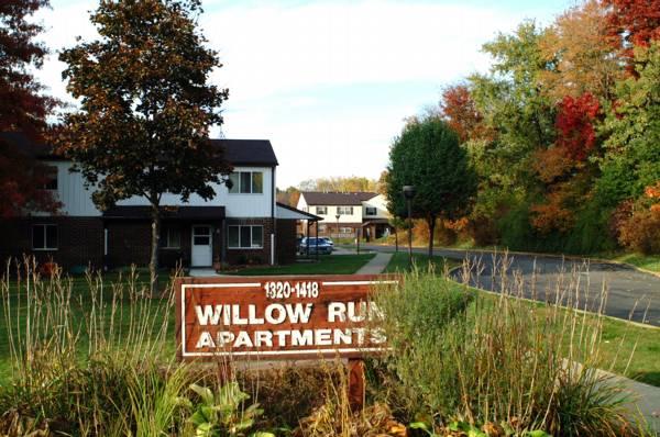 A wooden sign reading "Willow Run Apartments" stands in front of two-story apartment buildings and a paved driveway, surrounded by trees with autumn foliage.